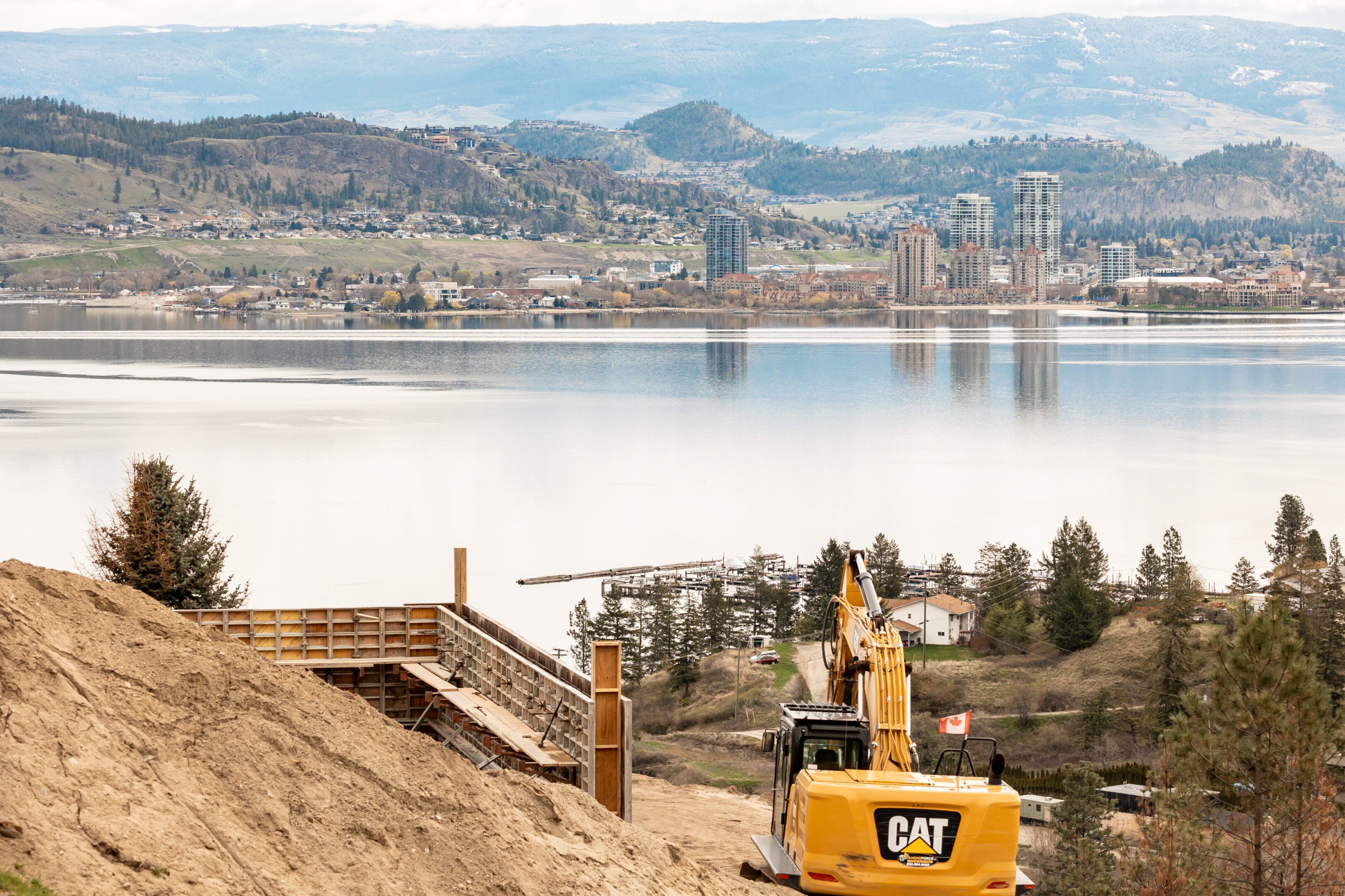 Excavator near lake with city background.