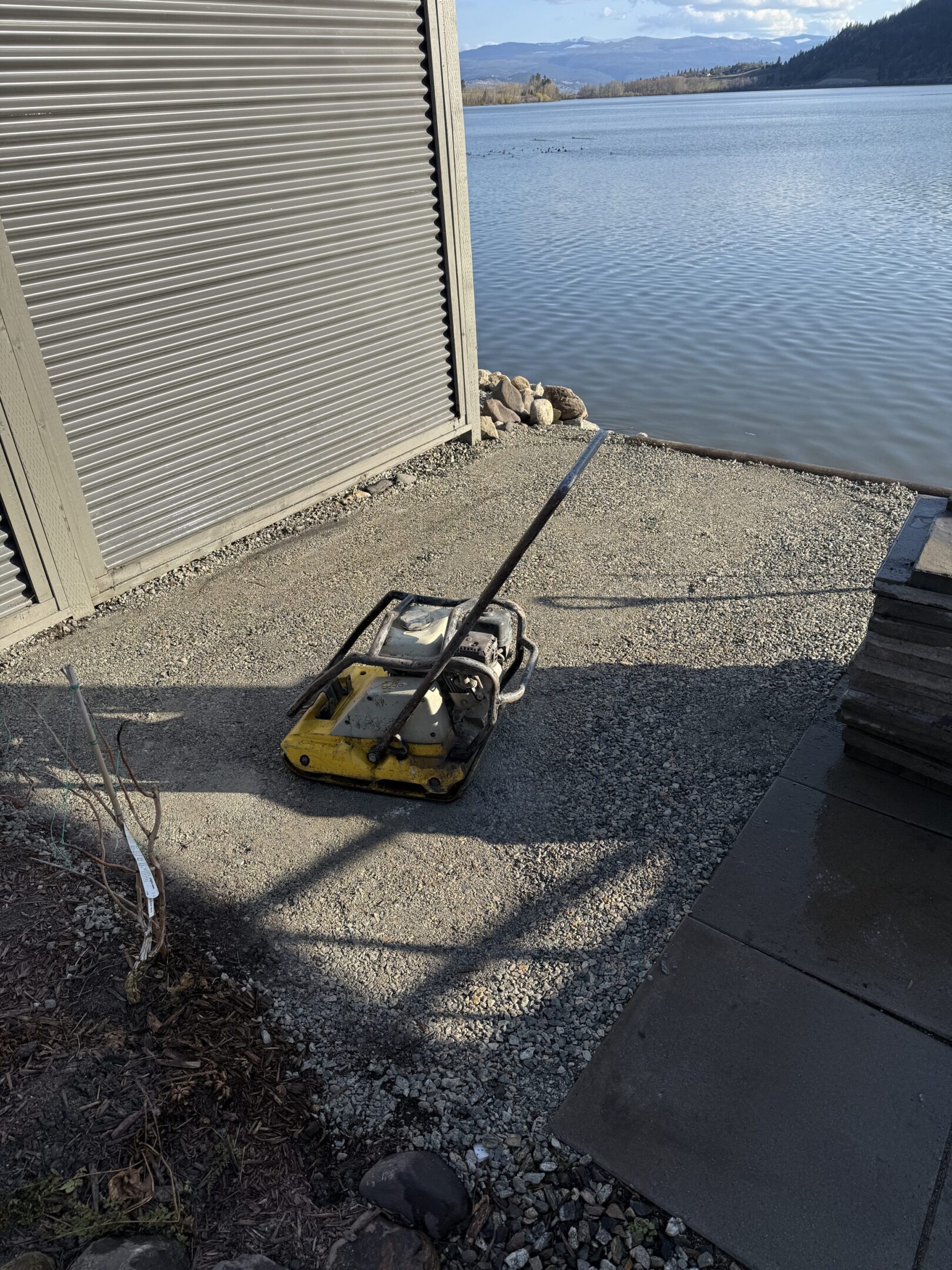 Compactor on gravel by a lakeside building.