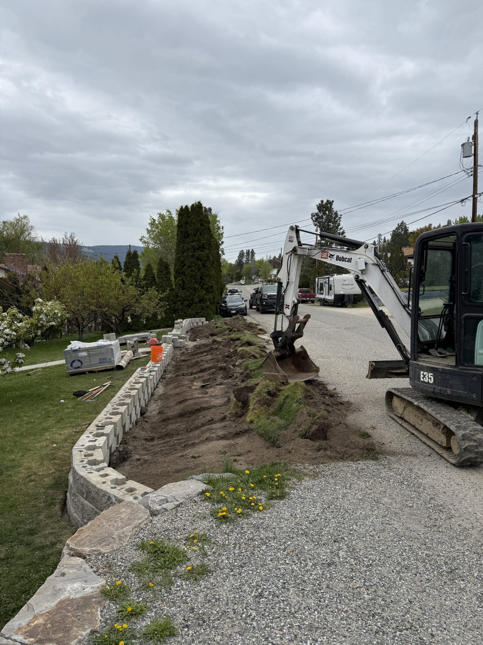 Excavator digging beside stone retaining wall.
