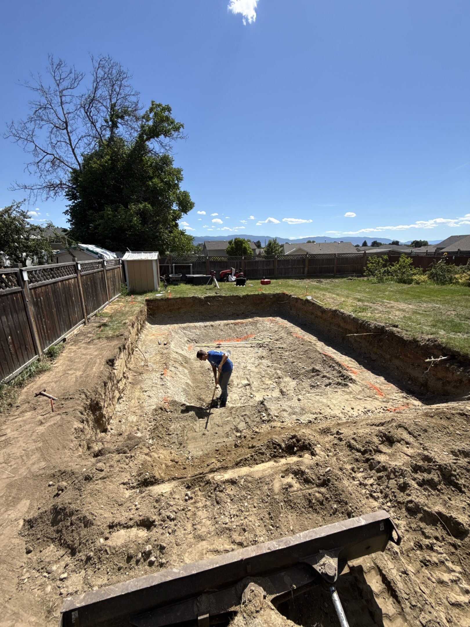 Person digging in large backyard excavation site.